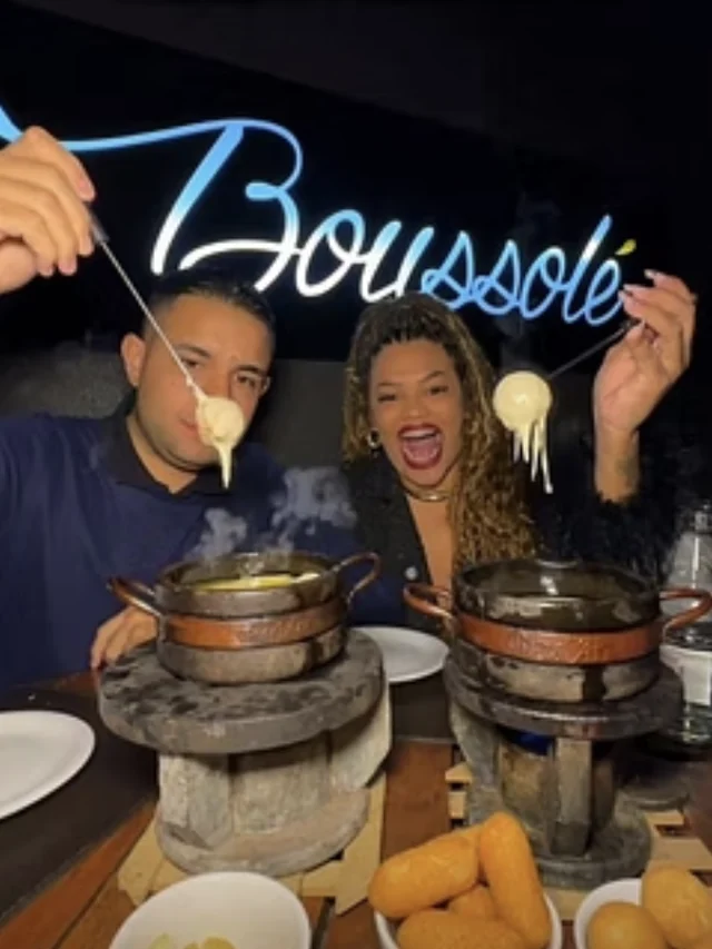 Boussolé Rooftop - clientes comendo fondue no salão, sob o letreiro neon da casa